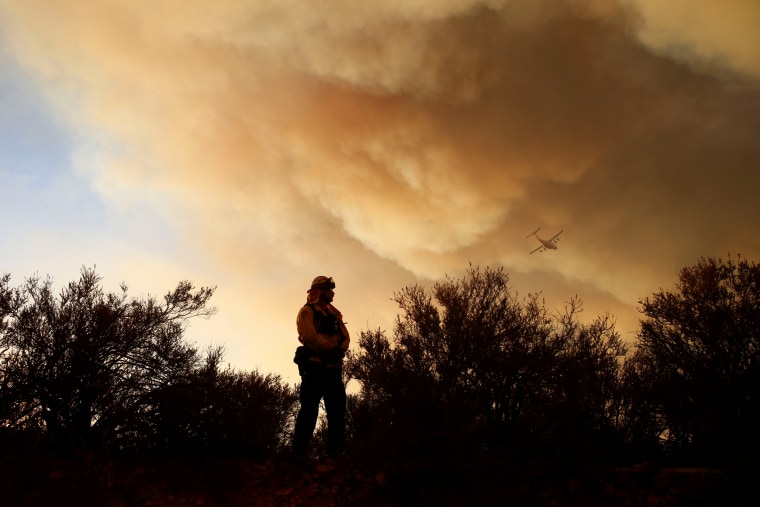 Image: A fire captain watches a fire's movement as an aircraft flies overhead during the Pilot Fire near in San Bernardino, California