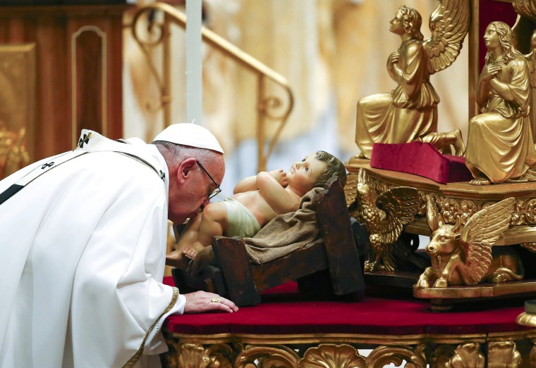 Image: Pope Francis kisses a statue of baby Jesus as he leads the Christmas night Mass in Saint Peter's Basilica at the Vatican