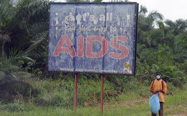 Image: A man stands next to an AIDS billboard as he cleans a street in Yaounde