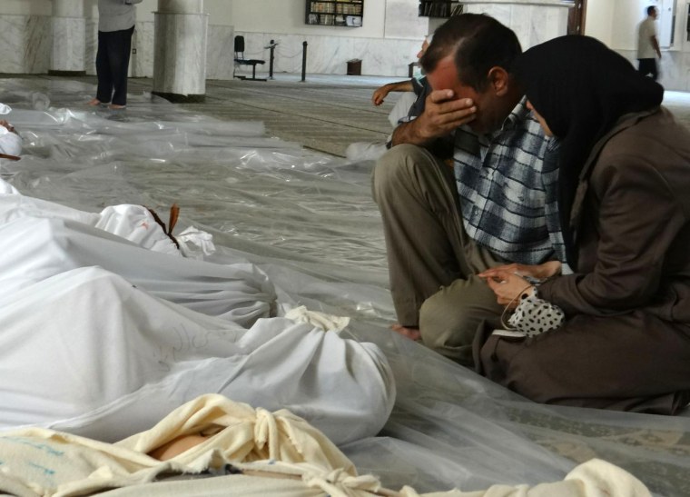 Image: A Syrian couple mourning in front of bodies wrapped in shrouds ahead of funerals following what Syrian rebels claim to be a toxic gas attack