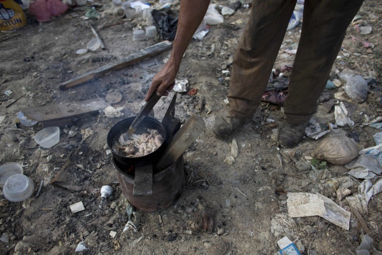 In this Nov. 1, 2016 photo, a man cooks chicken skin he found at the dump in Puerto Cabello, Venezuela, the port city where the majority of Venezuela's imported food arrives.