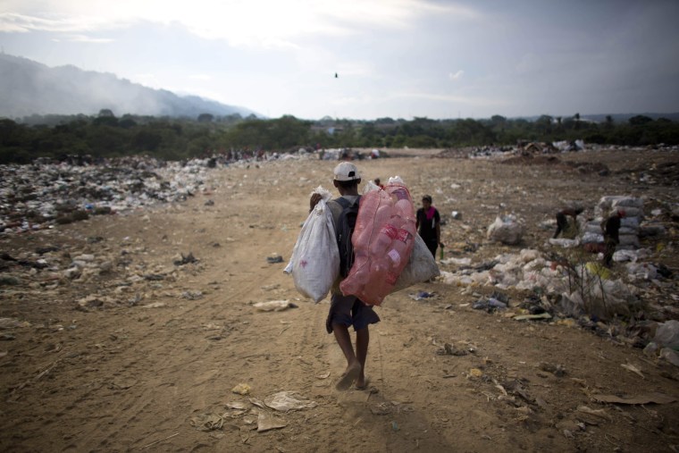 Image:In this Nov. 1, 2016 photo, a man carries bags of recyclable material he collected at the dump in Puerto Cabello, Venezuela.