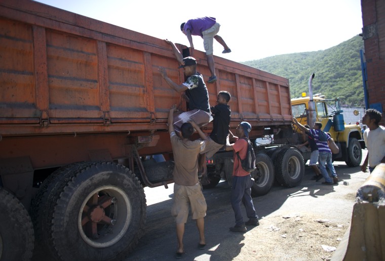 In this Nov. 14, 2016 photo, young men climb into an empty food truck, in search of leftover grain, as the vehicle comes to a slow stop outside the port in Puerto Cabello, Venezuela.