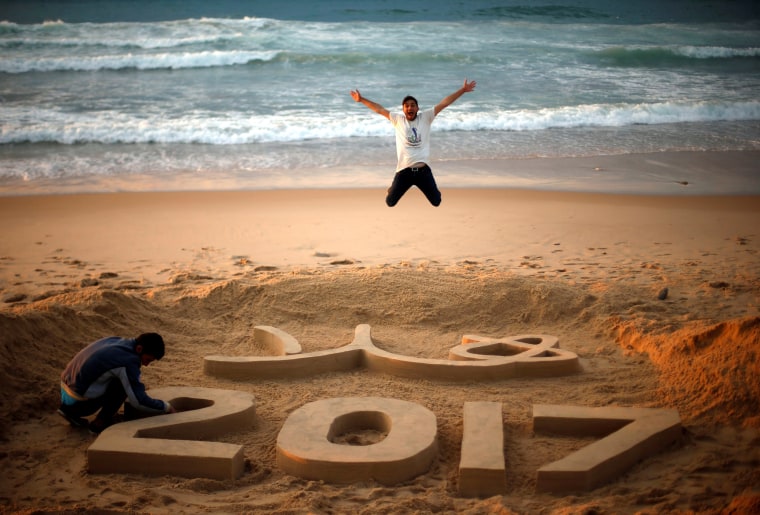 Image: Palestinian artist Yazed Abu Jarad puts the final touches on a sand sculpture that reads \"Welcome 2017\", as a man jumps, at a beach in the northern Gaza Strip