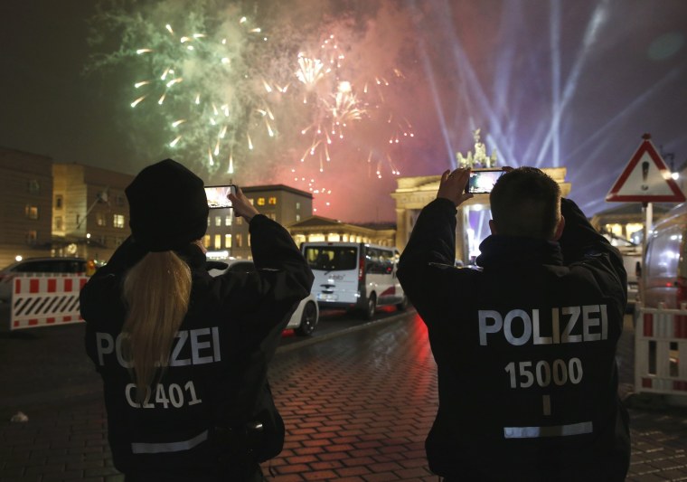 Image: German police officers take pictures as fireworks explode next to the Quadriga sculpture atop the Brandenburg gate during New Year celebrations in Berlin