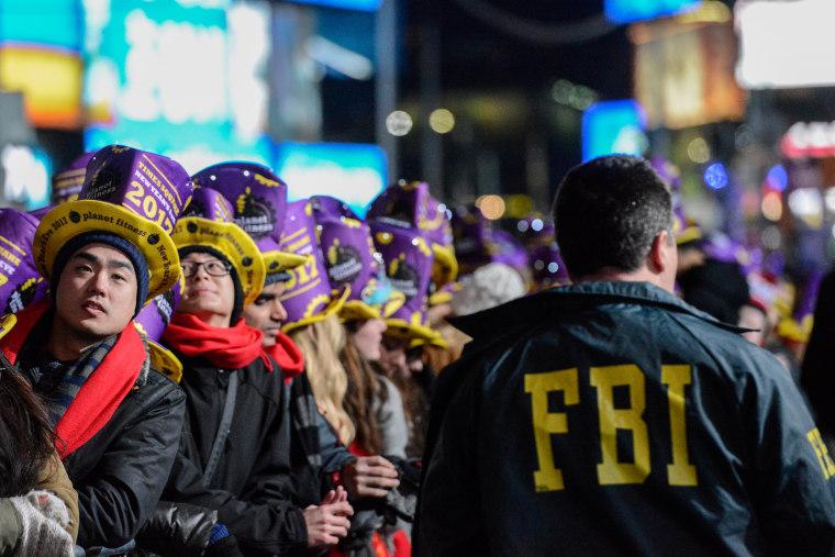 Image: An FBI agent walks past revelers gathered in Times Square on New Year's Eve in New York