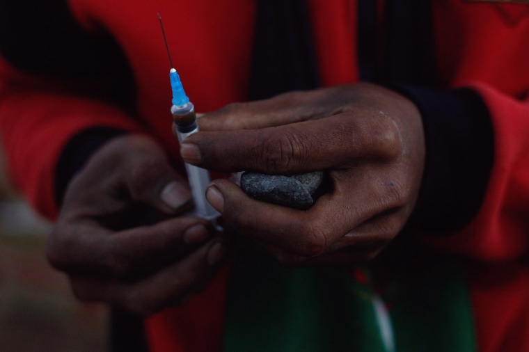 Image: A miner holds in his hands a jade stone and a syringe to use heroin at a mine dump at a Hpakant jade mine in Kachin state