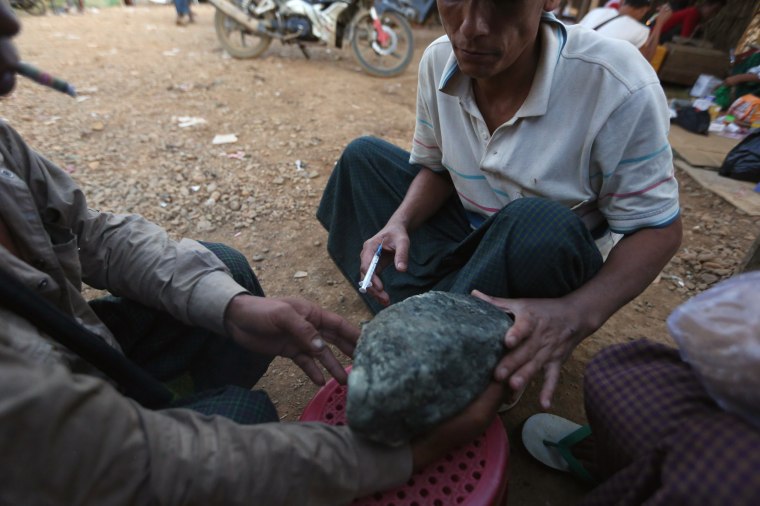 Image: Miners take a look at a jade stone while one of them injects himself heroin at a mine dump at a Hpakant jade mine in Kachin state