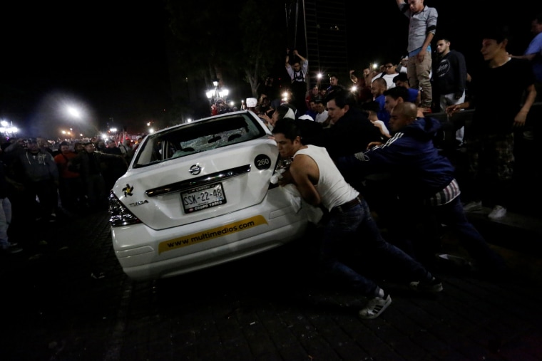 Image: Demonstrators push over a vehicle of Multimedios TV network during a protest against the rising prices of gasoline enforced by the Mexican government at the Macroplaza in Monterrey