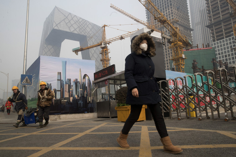 Image: A woman wearing a mask walks past a construction site as smog continues to choke Beijing