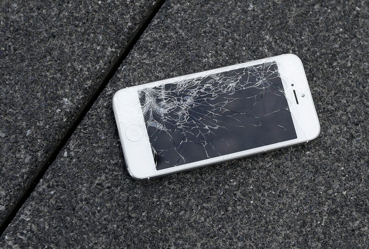 Image: A smartphone with a cracked screen lays on the ground