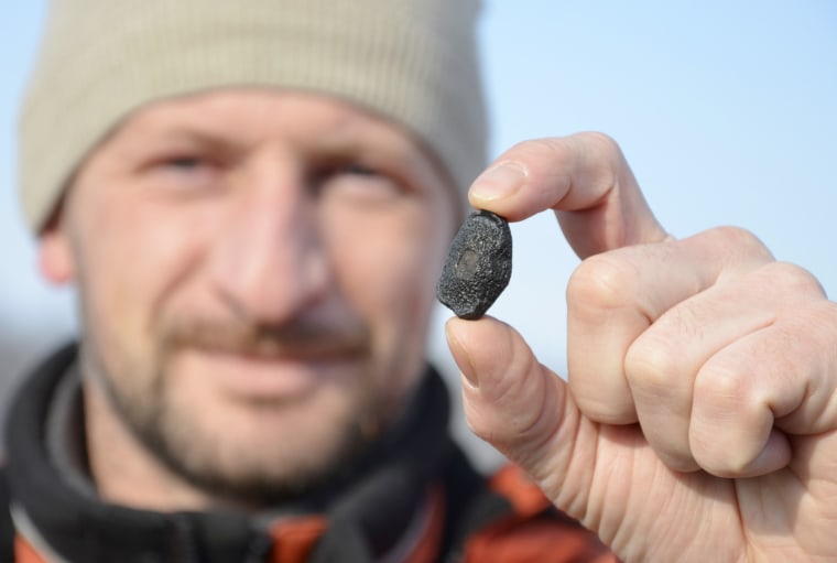 Image: A local resident shows a fragment thought to be part of a meteorite collected in a snow covered field in the Yetkulski region outside the Urals city of Chelyabinsk