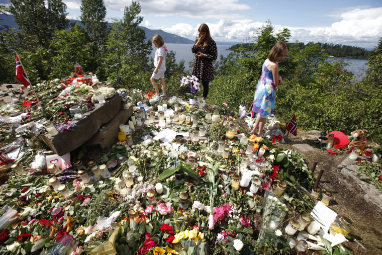 Image: Children stand at a temporary memorial site on the shore in front of Utoeya island