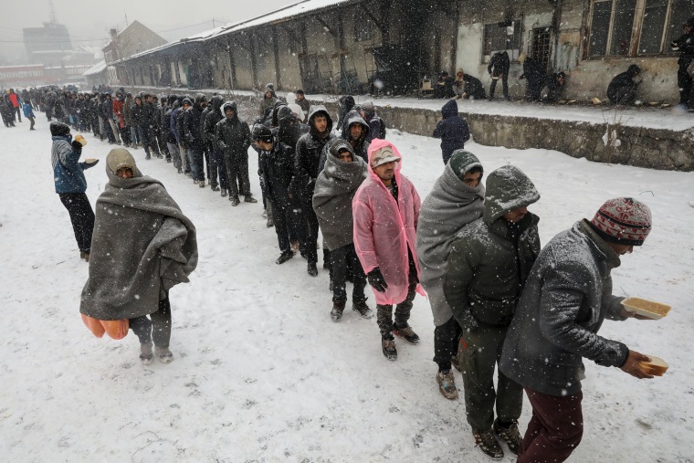 Image: Migrants stand in line to receive free food outside a derelict customs warehouse in Belgrade
