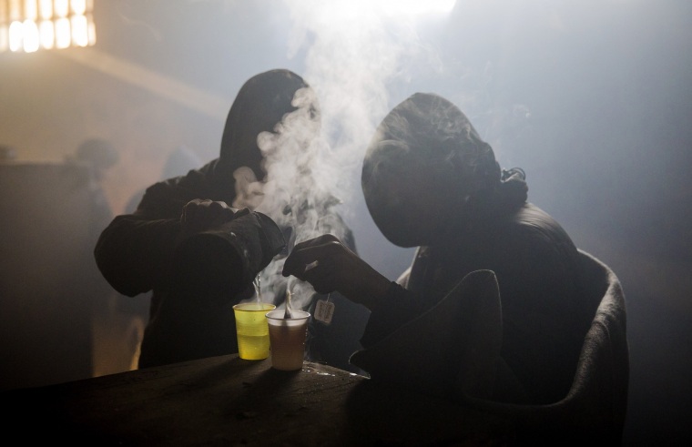 Image: Migrants drink tea at a makeshift shelter