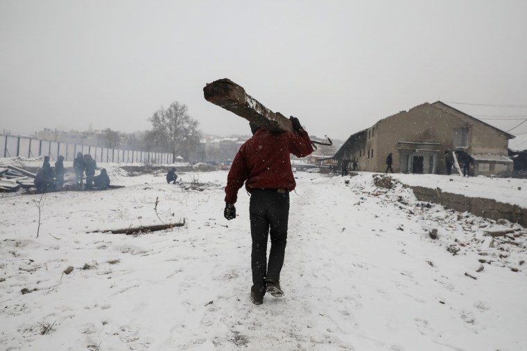 Image: A migrant carries a railway sleeper during a snowfall outside a derelict customs warehouse in Belgrade