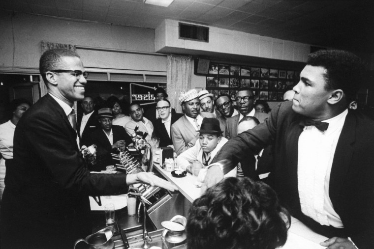 Image: Black Muslim leader Malcolm X, behind soda fountain, with  Muhammad Ali, while surrounded by jubilant fans after he beat Sonny Liston for the heavyweight championship of the world, March, 1964, in Miami, Florida.