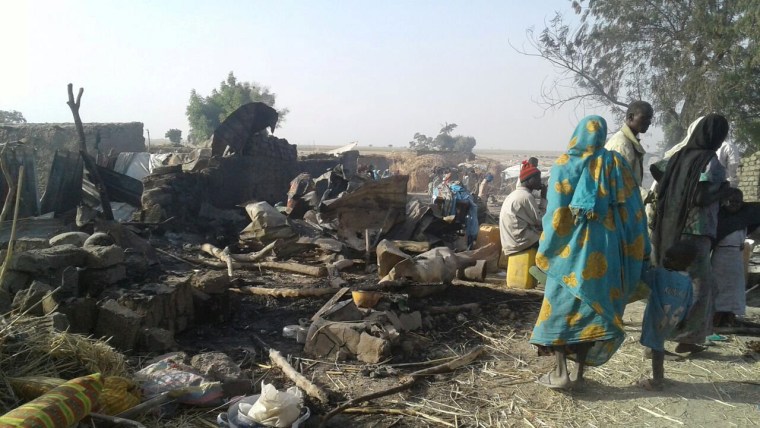 Image: People walk at the site after a bombing attack of an internally displaced persons camp in Rann