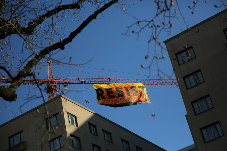 Image: Greenpeace activists hold an anti-Trump protest as they display a banner reading 'Resist' from a construction crane near the White House in downtown Washington