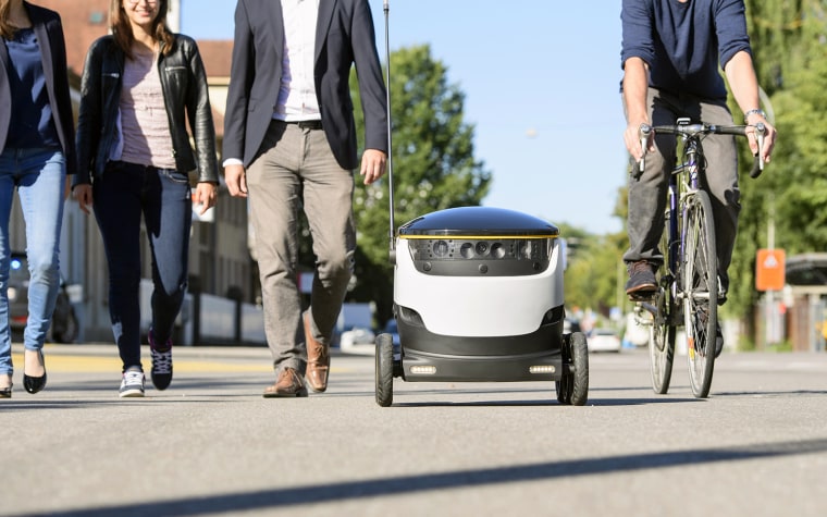 Pedestrians pass a Starship delivery robot.