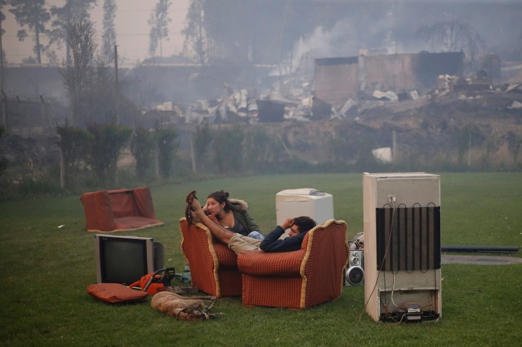 Image: A young couple rest in a football field after a forest fire devastated Santa Olga