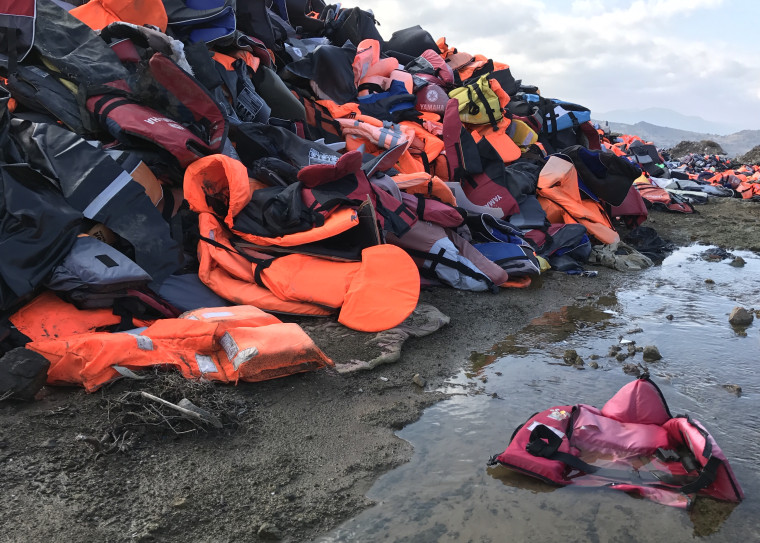 Image: A little pink life jacket lies in a giant dump of thousands of life jackets