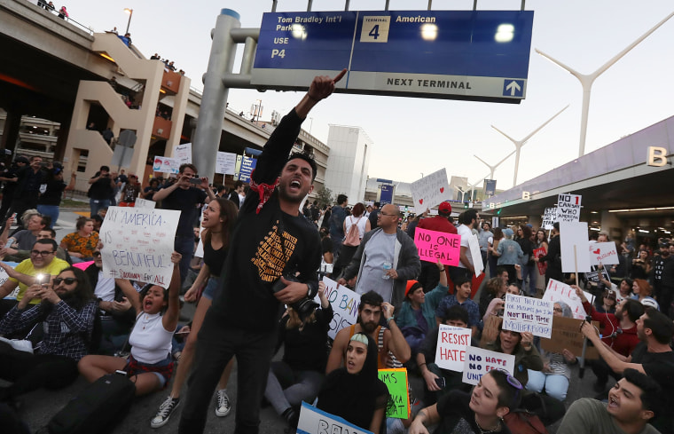 Image: Protesters chant as they block a road during a demonstration against the immigration ban imposed