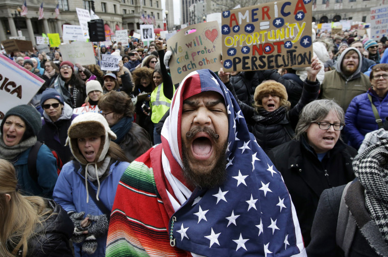 Image: Izzy Berdan, of Boston, center, wears an American flags as he chants slogans with other demonstrators during a rally