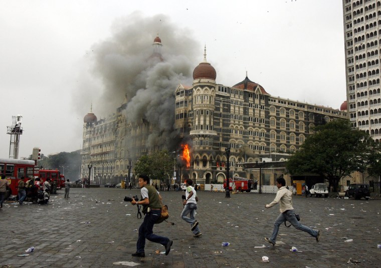 Image: Photographers run past a burning Taj Mahal Hotel during a gun battle in Mumbai