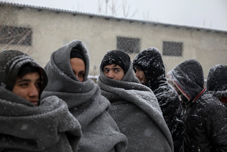 Image: Migrants wait in line to receive free food during a snowfall outside a derelict customs warehouse in Belgrade