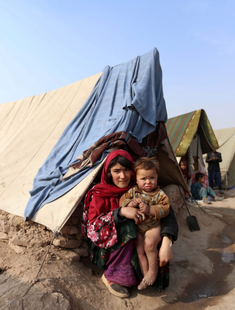 Image: People driven from their homes by violence sit in front of a tent 