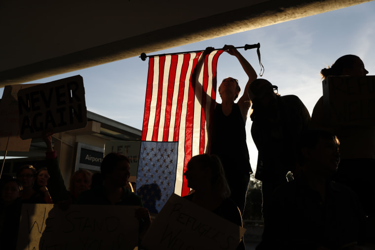 Image: A demonstrator holds an American flag during a rally at SFO
