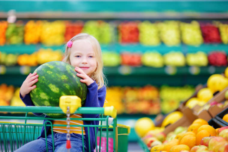 Little girl holding watermelon in shopping cart