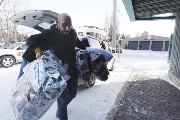 Image: A person brings blankets into a community hall for refugees