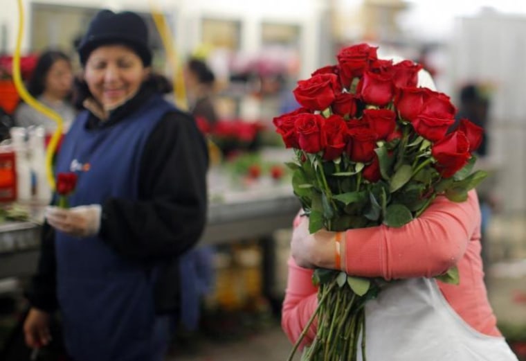A worker carries an armload of red roses at Winston Flowers in Boston