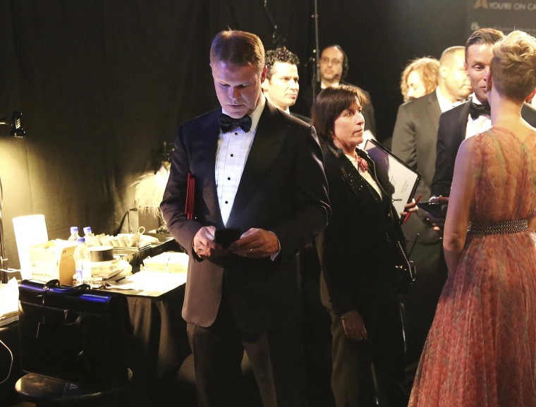 Image: Brian Cullinan  holds red envelopes under his arm while using his cell phone backstage at the Oscars