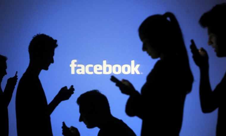 Image: People pose with laptops in front of projection of Facebook logo in this picture illustration taken in Zenica