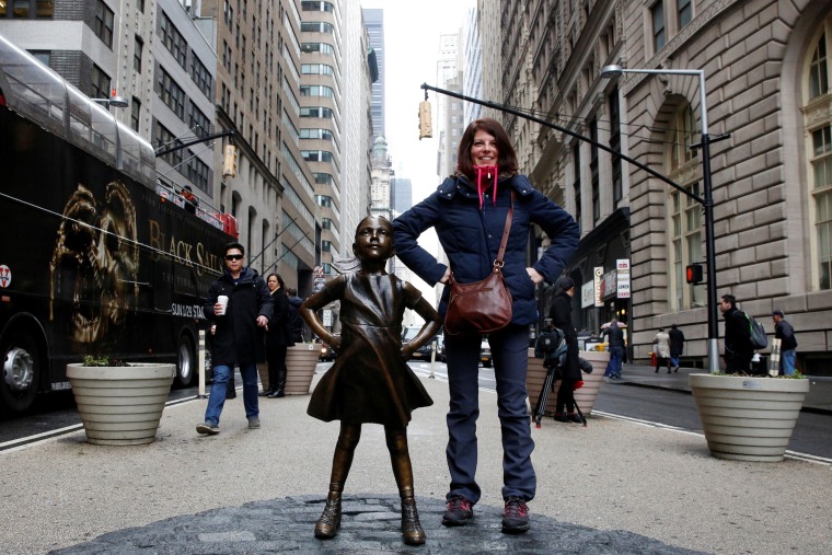 Image: A woman poses next to a statue of a girl facing the Wall St. Bull, as part of a campaign by U.S. fund manager State Street to push companies to put women on their boards, in the financial district in New York