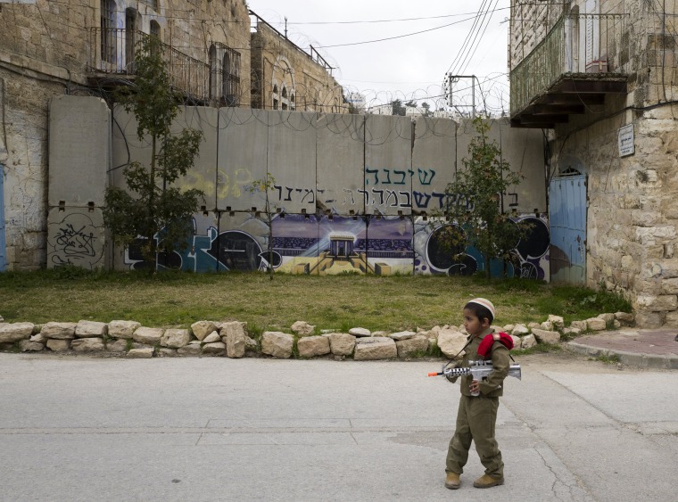 Image: A young Jewish boy dressed in an army costumes stops before a separation wall blocking a street during the annual Purim parade in Hebron.
