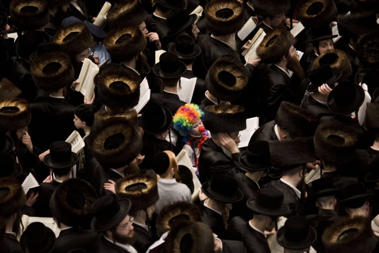 Image: An Ultra Orthodox Jewish child dressed as a clown stands among men reading from the Book of Esther during a prayer for the Jewish Holiday of Purim in the Mea Shaarim neighborhood in Jerusalem, Israel.
