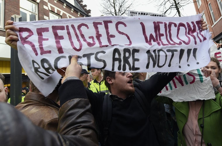 Image: A protester with a banner reading "Refugees welcome, racists are