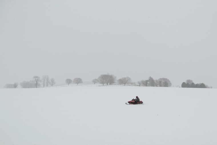 Image: A person rides a snowmobile through a field in Gap, Pa.