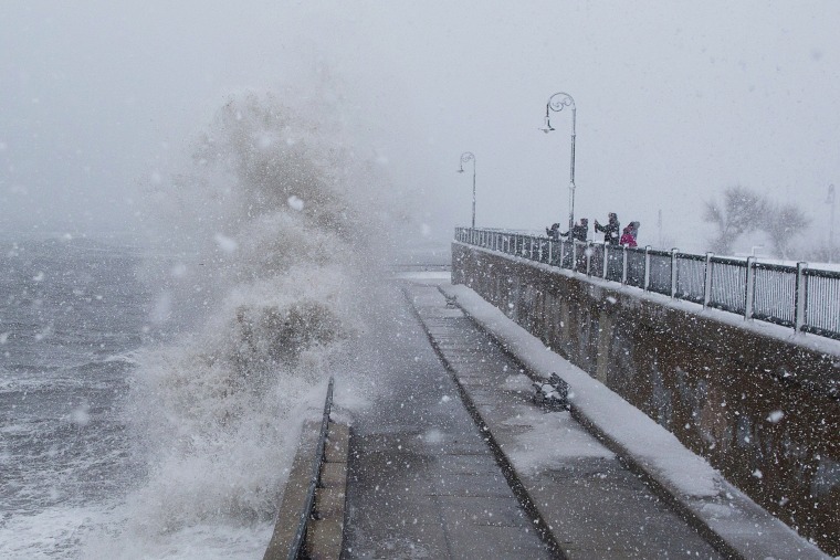 Image: People watch as waves crash over the seawall along Lynn Shore Drive