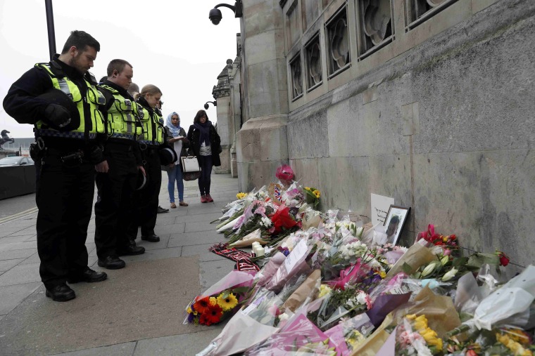 Image: Police officers and civilians look at flowers left near Westminster Bridge in London