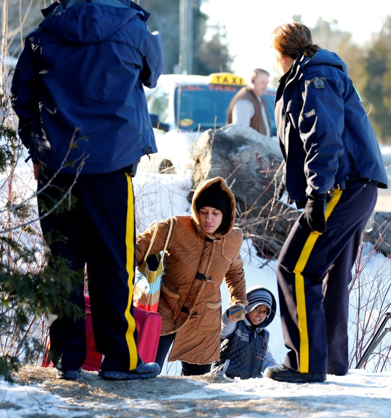 Image: A woman and her child, who claimed to be from Sudan, are met by Royal Canadian Mounted Police (RCMP) officers after they crossed the U.S.-Canada border illegally leading into Hemmingford, Quebec