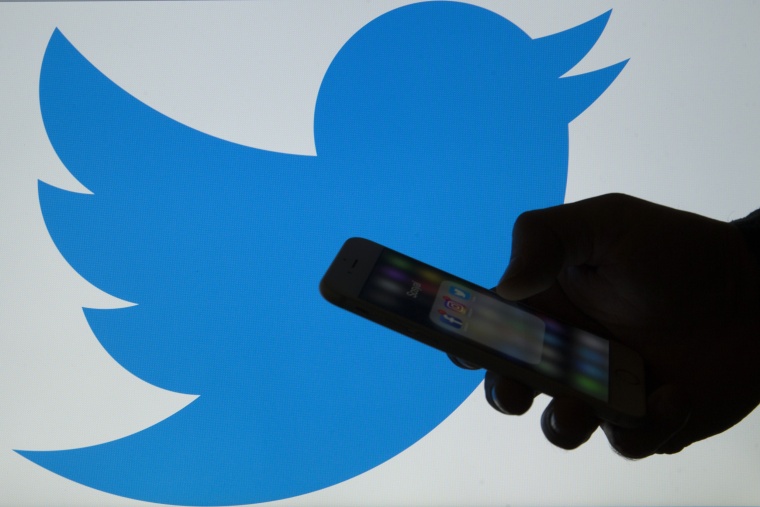 Image: A man holds a cellphone in front of a twitter logo