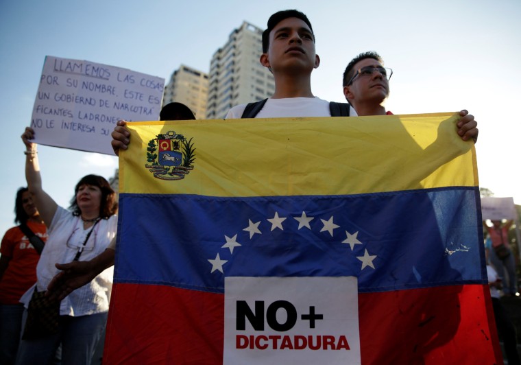 Image: An opposition supporter holds a Venezuelan flag with a sign that reads "No more dictatorship" during a protest against Venezuelan President Nicolas Maduro's government, in Caracas