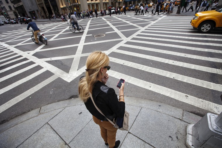 Image: A woman uses her Apple iPhone while waiting to cross 5th Avenue in New York