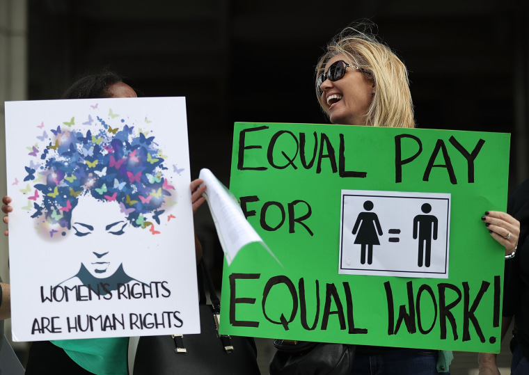 Image: Protesters hold signs during a rally to support equal pay for equal work