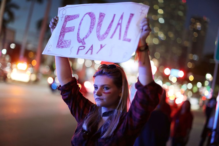 Image: A protester holds a sign reading "Equal Pay" as she joins with others during A Day Without A Woman demonstration